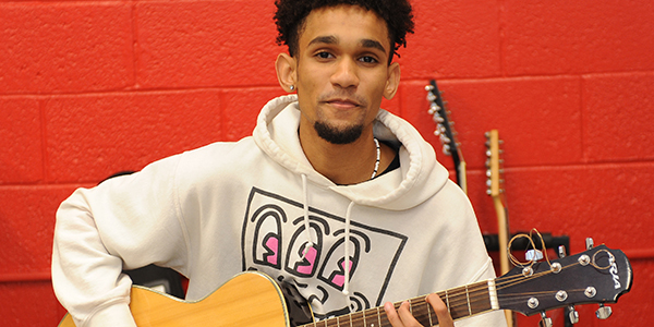 A student smiling holding a guitar.